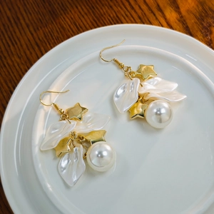 Detail of elegant gold star and white petal pearl drop earrings on ceramic tray