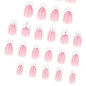 French almond press-on nails in nude pink with white tips, pearls, and 3D bow accents
