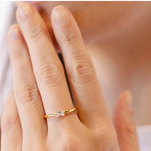 Close-up of minimalist gold-plated ring with emerald-cut zircon on female finger