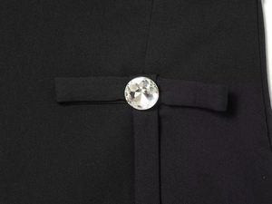 Detailed macro view of a large sparkling rhinestone button on a black textured fabric vest