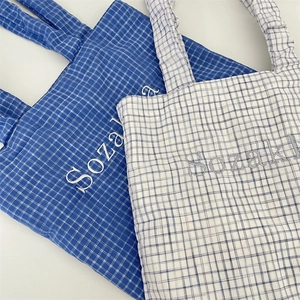 Detail view of woven checkered tote bags with Sozaki embroidery in blue and white colors