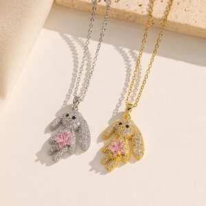 Silver and gold rabbit pendant necklaces with pink star stones on a textured surface