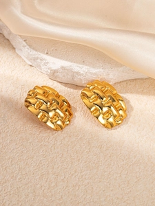 Détail macro de boucles d'oreilles tissées dorées sur fond de soie et de pierre