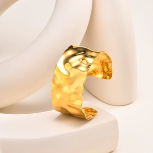 Dettaglio del bracciale aperto dorato a forma di C con texture in metallo martellato