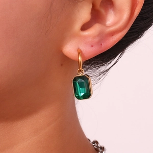 Close-up of model wearing rectangular emerald green zircon pendant earrings in 18k gold