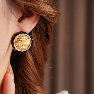 Close-up of golden and black circular woven earrings worn by a model in soft lighting