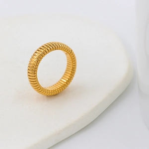 Macro shot of a golden textured ring with horizontal ridges on a white ceramic display