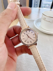 Detailed view of champagne leather strap watch with rhinestone bezel worn on wrist