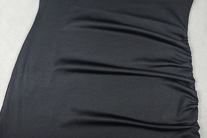 Macro detail of the side ruching and pleated texture on this black slim-fit dress