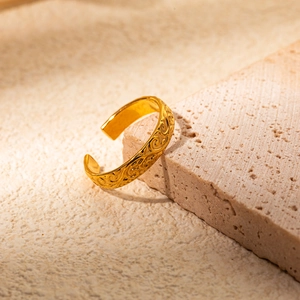 Fashionable gold open ring with embossed vintage scroll pattern on textured stone background