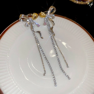 Detail shot of silver tassel earrings with yellow and pink zircons on a white ceramic plate