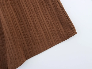 Close-up of brown fabric texture with vertical pleated details and stitching on women's set