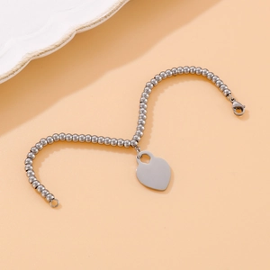 Detail view of silver beaded chain bracelet with a signature heart pendant on warm background