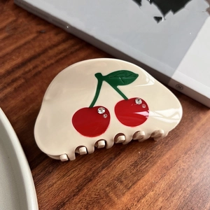 Close-up of cream acetate hair claw clip with red cherry motif and sparkling rhinestones