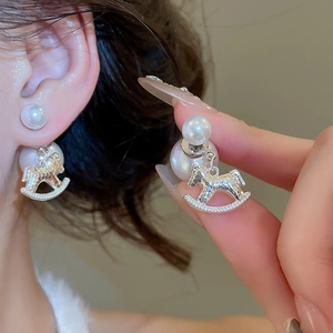 Close-up of pearl stud earrings with silver rocking horse charms on female model