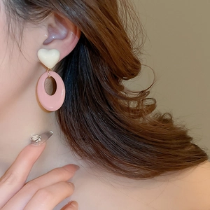 Close-up of white heart and pink oval resin earrings worn by a model in soft lighting