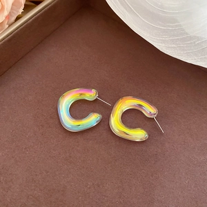 Macro shot of iridescent acrylic C-shape hoop earrings on a decorative brown tray