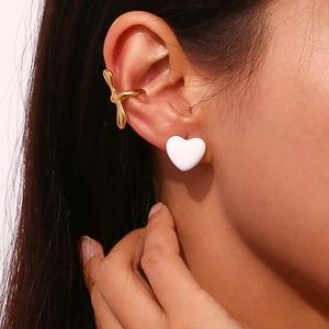 Close-up of model wearing white heart stud earrings and gold-plated clip-on ear cuff