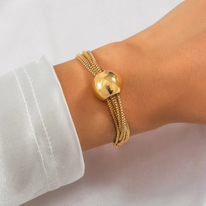 Detail of layered gold chain bracelet with large polished bead on model wrist