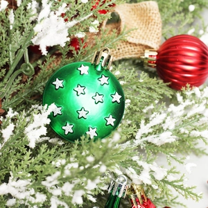 Red and green Christmas ball ornaments with silver stars on snowy pine branches