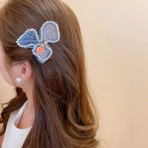 Detail of a blue butterfly hair clip with white pearls and beads on wavy brown hair
