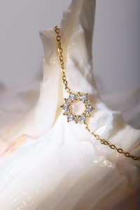 Macro detail of 18K gold necklace with sunburst pendant and white zirconia stones