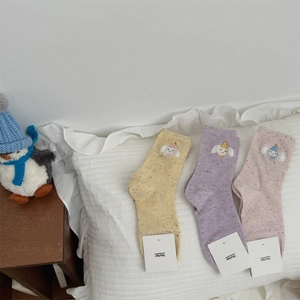 Detailed view of colorful speckled cotton socks with cartoon embroidery on ruffled pillow