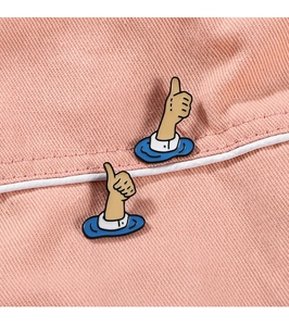 Close-up of a cartoon thumb up brooch pinned on pink twill fabric with visible texture