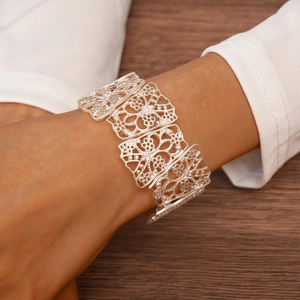 Close-up of a silver hollow floral cuff bracelet with matte metallic finish worn on wrist