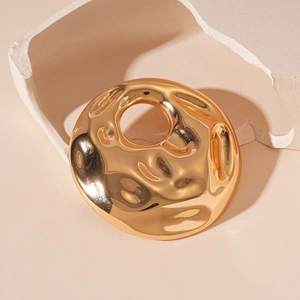 Macro detail of golden circular brooch featuring unique hammered texture and hollow center