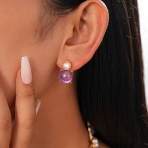 Close-up of vintage gold earrings with white pearl and round purple gemstone on model