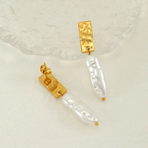 Détails de boucles d'oreilles perles baroques et métal doré martelé sur tissu beige