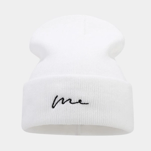 Close-up of white knit beanie featuring black 'me' script embroidery on the folded cuff