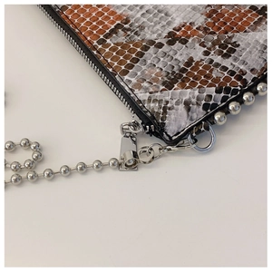 Detailed macro view of snake pattern leather flap with silver ball chain and zipper