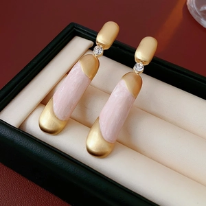 Dettaglio di orecchini lunghi oro opaco e rosa con strass in una scatola per gioielli verde