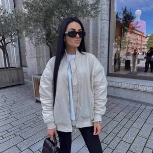 Oversized cream bomber jacket for women styled with black leggings in outdoor setting