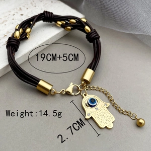 Leather wrap bracelet with gold Hamsa Hand and Evil Eye charm on marble background