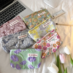 Flat lay of floral jacquard pouches in various colors on a white textured fabric background