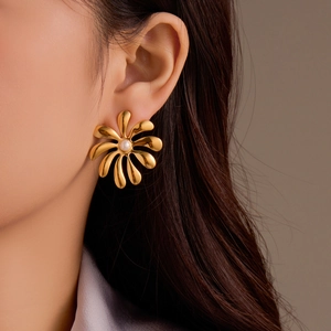 Close-up of golden flower stud earring with a white pearl on a model's ear