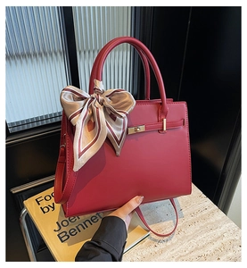 Detail of red leather tote bag featuring golden turn-lock clasp and decorative silk scarf