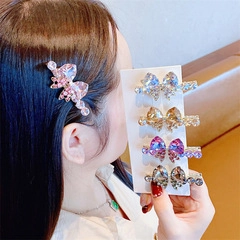 Detail showing four crystal bow hair clips in pink, champagne, purple, and grey colors