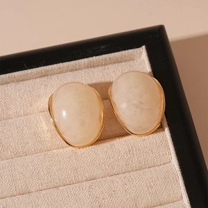 Detailed macro view of retro cream resin oval earrings with elegant gold metal framing