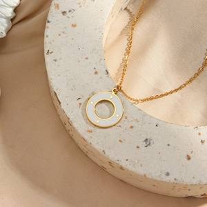Detail of gold necklace with white enamel circle pendant on soft silk and stone base