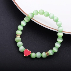 Detail of light green cat eye beaded bracelet with a red enamel heart charm on black background
