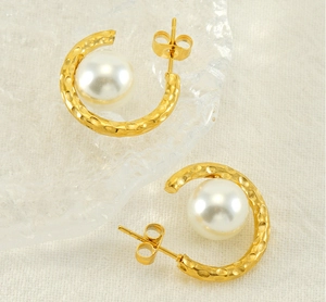 Détail de boucles d'oreilles C dorées martelées avec grandes perles sur fond en lin