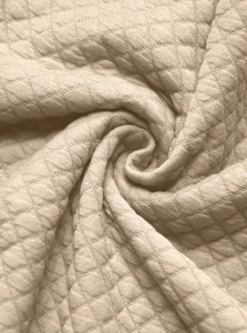 Detailed close-up of beige quilted fabric with a soft diamond waffle texture and weave