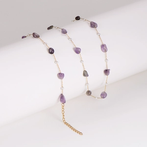 Golden necklace with irregular purple gemstones and white pearls on a white stand