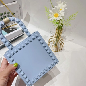 Close-up of light blue PVC mini square bag with golden pyramid studs detail