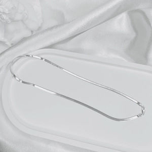 Close-up of a silver flat snake chain necklace on white marble with a lobster clasp
