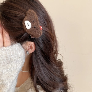 Detailed view of a brown plush bear hair clip styled on wavy dark brown hair